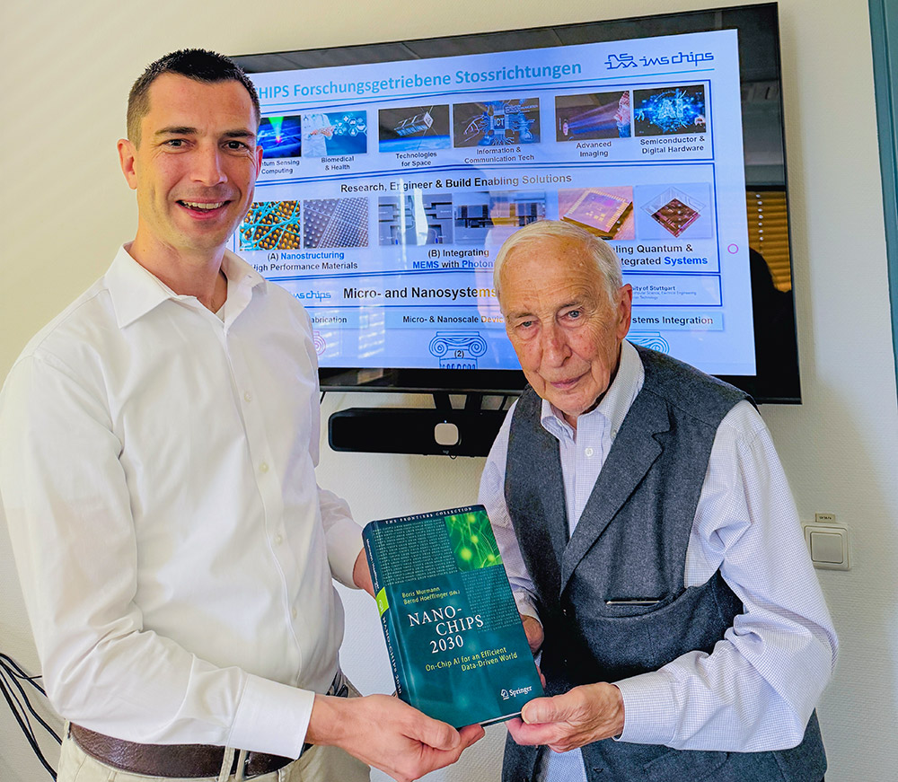 Auf dem Bild stehen links Niels Quack, der aktuelle Institutsleiter von IMS CHIPS, rechts Bernd Höfflinger, der erste Institutsleiter. Herr Höfflinger überreicht seine jüngste Publikation an Herrn Quack. Im Hintergrund ist eine wissenschaftliche Präsentationsfolie zu Zukunftsfeldern zu sehen.